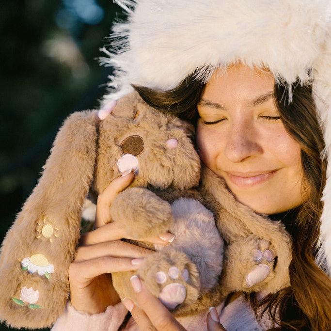 Woman wearing a fluffy white hooded coat holding a plush bunny toy outdoors.